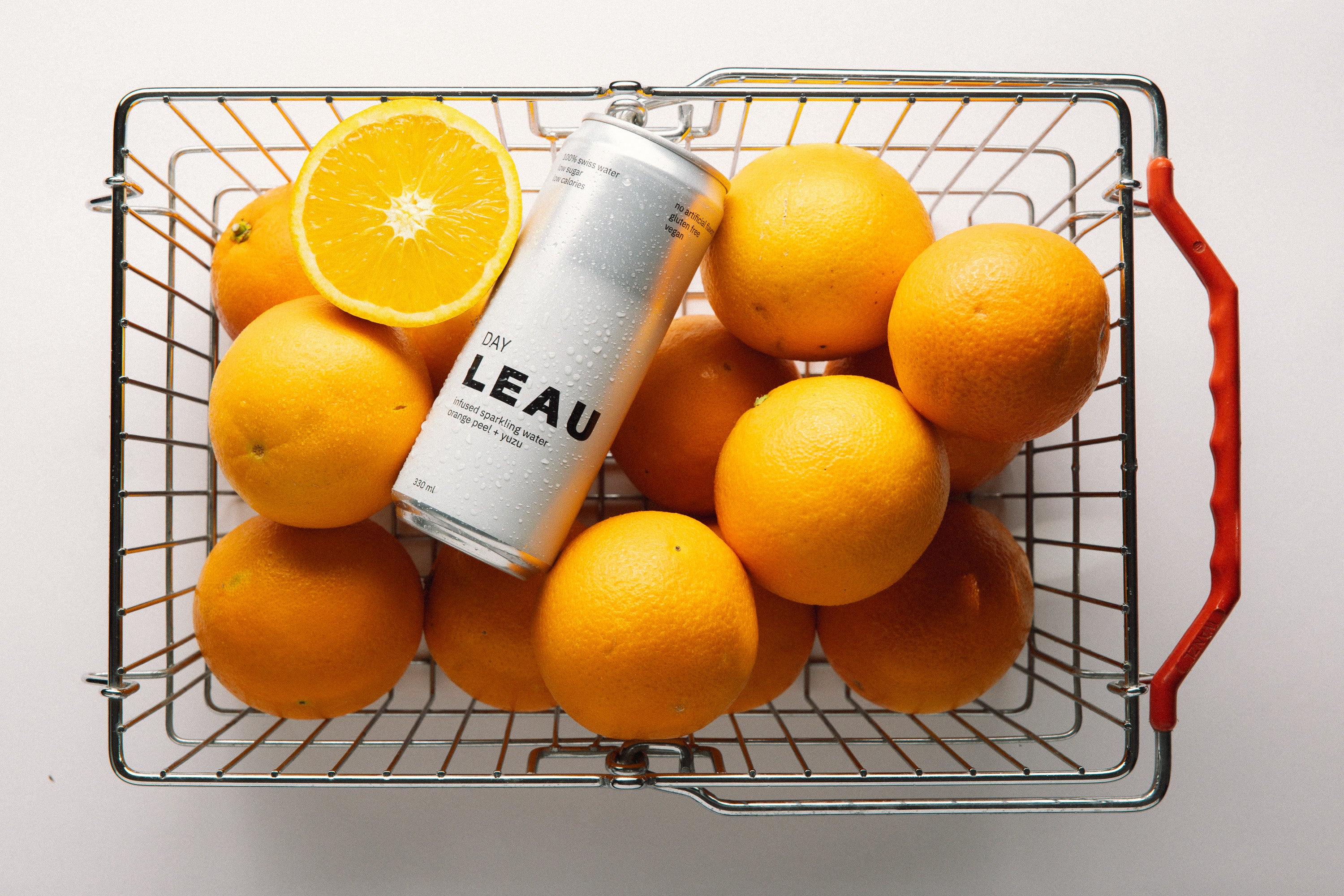 Can of LEAU DAY with oranges in a wire basket on a white background