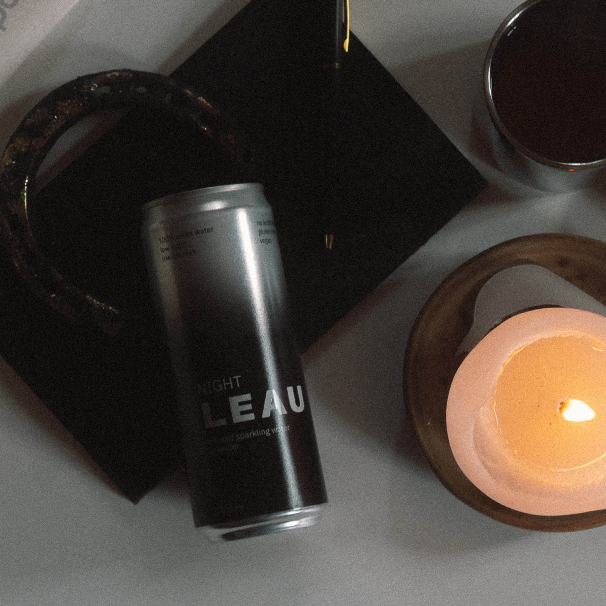 Black can labeled 'LEAU' next to a lit candle on a gray surface