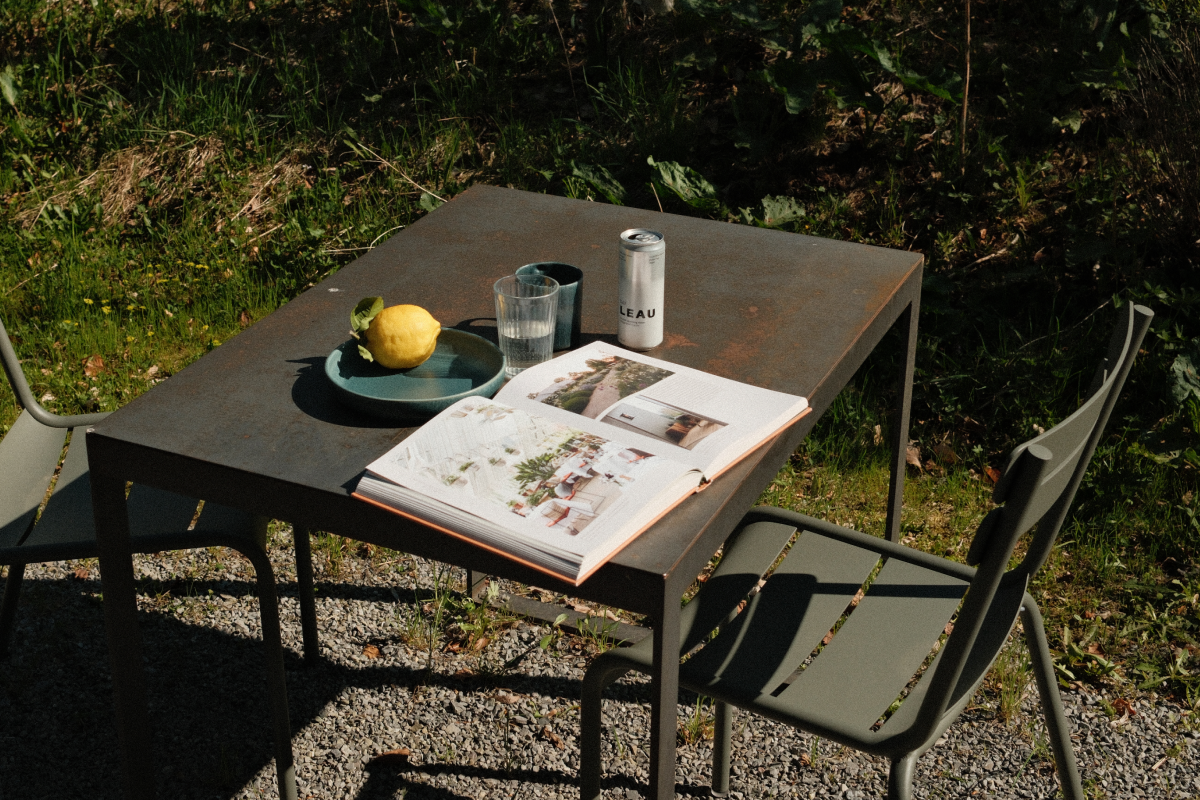 Outdoor table with a book, glass, a can of LEAU DAY and lemon on a natural background