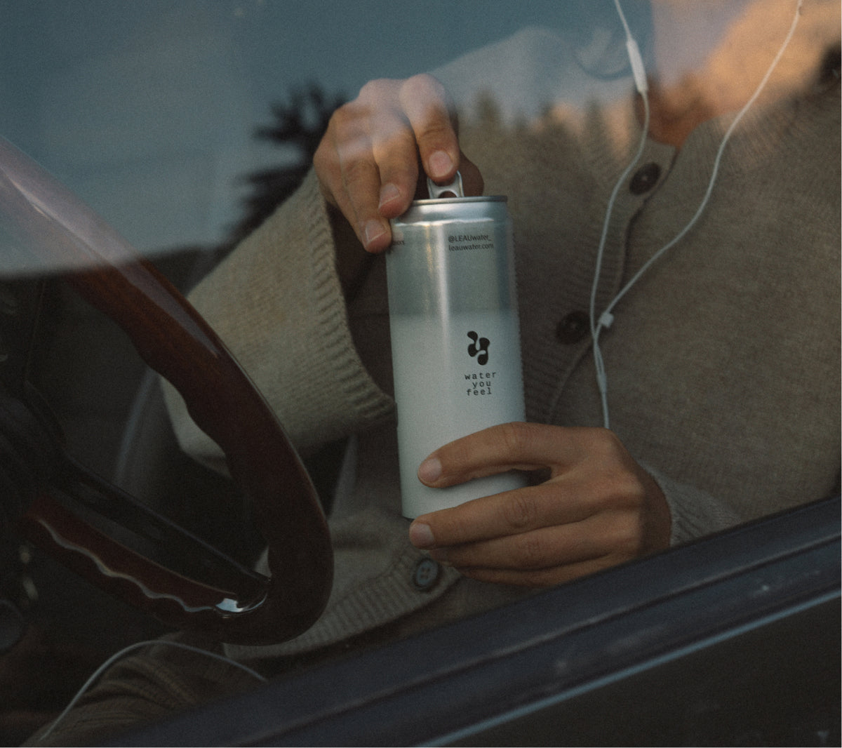 Woman opening a can through a car window that says water you feel.